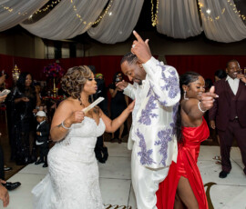 Bride in white gown dancing with guests at an indoor Louisiana wedding under draped fabric and string lights.