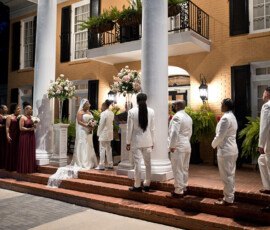 Bride and groom wed at night on brick steps with bridesmaids in burgundy, groomsmen in white, by a grand Gulf South building.