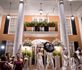 Louisiana wedding party celebrates outside white-columned building with gold streamers, umbrellas, and vibrant burgundy bridesmaids.