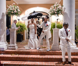 Bride and groom in white celebrate on steps with guests, confetti, and flowers at a festive Louisiana nighttime wedding.
