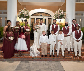 Wedding party on steps: bride in white, groom in suit, burgundy bridesmaids and groomsmen, flower girls and ring bearers in white.