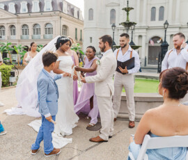 Bride and groom at outdoor Louisiana wedding with smiling guests, bouquet, and veil in festive atmosphere.