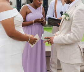 Bride and groom hold vow books at an outdoor Louisiana wedding, with bridesmaid in lavender and officiant behind them.