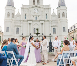 Bride and groom exchange vows outside a white church, with bridesmaids in lavender and groomsmen in beige at a Gulf South wedding.
