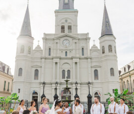 Outdoor Louisiana wedding in front of a historic church with tall spires, bride and groom at the altar, guests on white chairs.