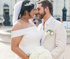 Bride and groom smile outdoors in New Orleans, holding white roses at their Gulf South wedding.