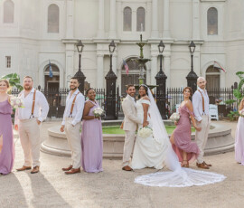 Bride and groom pose with their wedding party in front of a historic building after a Gulf South ceremony.