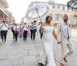 Bride and groom lead a lively city parade with musicians, guests, and decorated umbrellas for vibrant wedding inspiration.