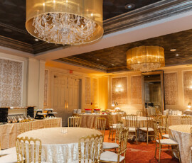 Elegant Louisiana banquet room with round tables, gold chairs, chandeliers, cream linens, and a buffet—ideal for weddings.
