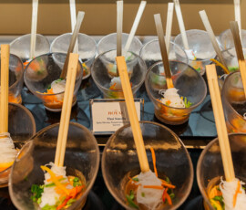 Clear bowls of Thai noodles with vegetables and chopsticks are arranged in rows, labeled “Thai Noodle” for a wedding reception.