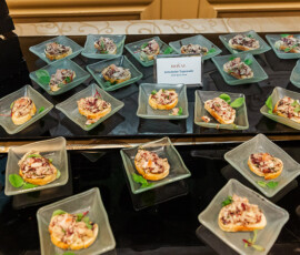 Mini glass dishes with artichoke tapenade on crackers, arranged on a black tray with a label card—ideal for Louisiana weddings.