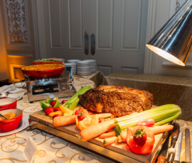 Louisiana wedding buffet with roast, carrots, celery, tomatoes, strawberries, dip, and macaroni under warm lighting.