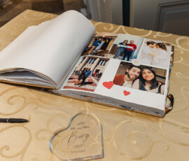 Open photo album on gold-patterned table with couple’s photos, red heart stickers, pen, and engraved wedding plaque.