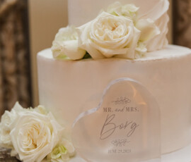 White wedding cake with white roses beside a heart plaque reading Mr. and Mrs. Borg, June 29, 2021—elegant wedding inspiration.