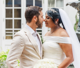 Bride in white gown and groom in light suit share a joyful moment outdoors with white roses at a classic Louisiana wedding.