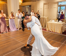 Bride and groom dance dip on a wooden floor at their Louisiana wedding, guests smiling and clapping nearby.