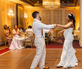 Bride and groom dance in a warmly lit ballroom as elegantly dressed guests watch and applaud, Louisiana wedding inspiration.
