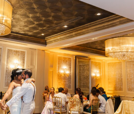 A couple’s first dance in a warmly lit, elegant Gulf South wedding ballroom with chandeliers and seated guests.