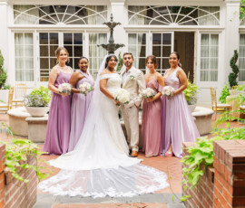 Bride and groom with four bridesmaids in pastel dresses pose by a fountain at their joyful Louisiana courtyard wedding.