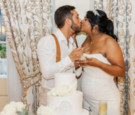 Bride and groom kiss and feed each other cake beside a white tiered cake at their Gulf South wedding reception.
