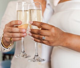 A couple in white attire clink champagne glasses, showcasing an engagement ring and New Orleans wedding romance.
