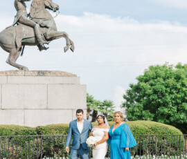 Bride in white dress walks with man and woman in blue near equestrian statue and greenery, New Orleans wedding inspiration.