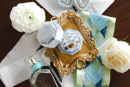Wedding rings in a blue velvet box on a gold tray, surrounded by white flowers and ribbon, at a Louisiana wedding.