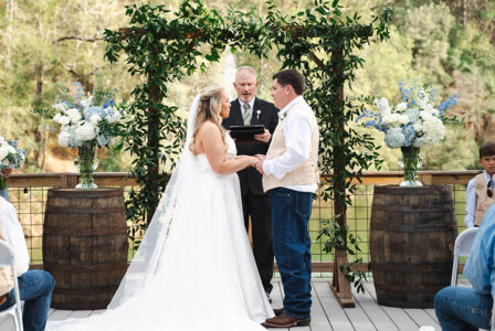 Bride and groom hold hands at an outdoor New Orleans wedding, with floral altar and guests seated on both sides.