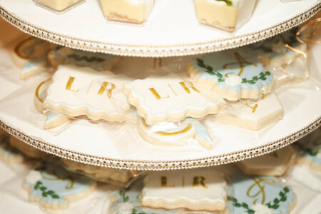 Gold lettered LIR iced cookies in clear bags on a tiered tray, with assorted cookies and dessert cups for New Orleans weddings.