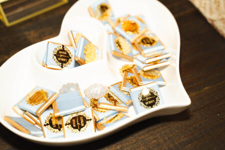 Gold and blue chocolates with ornate labels on a white heart-shaped dish atop dark wood, ideal for New Orleans weddings.