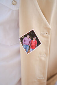 Beige jacket close-up with a pinned photo of two smiling men at a wedding, one in pink, one in red shirts and jeans.
