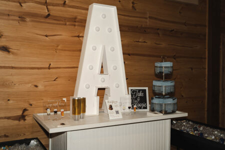 White bar with illuminated A, blue cups, drink dispensers, and rustic wood wall set the scene for a Louisiana wedding.