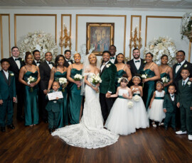 Full wedding party portrait with bride, groom, bridesmaids in emerald dresses, groomsmen in black tuxedos, and flower girls in white dresses