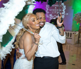 Bride and groom smiling under second line umbrellas on dance floor with colorful lighting during lively wedding reception