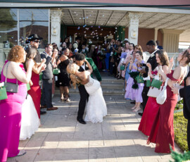 Bride and groom dip kiss outside venue surrounded by guests blowing bubbles during joyful wedding exit celebration