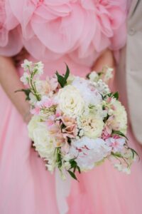 Person in a pink ruffled dress with white and pale pink bouquet stands next to someone in beige—stylish wedding inspiration.