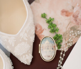 Close-up of a white lace shoe, necklace, greenery, floral paper, and Rome locket—elegant Louisiana wedding details.
