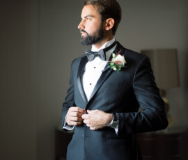 A man in a black tuxedo with a bow tie adjusts his jacket indoors, evoking classic wedding style for a Louisiana celebration.