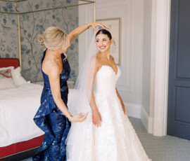 A woman in a navy gown fixes a smiling bride’s veil in a bright bedroom before their New Orleans wedding ceremony.