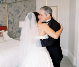 Bride in white dress hugs older man in tuxedo, both emotional and happy, sharing a warm moment before the ceremony.