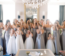 Bridesmaids in silver and flower girls in white playfully cover their faces indoors, perfect for joyful Louisiana wedding inspo.