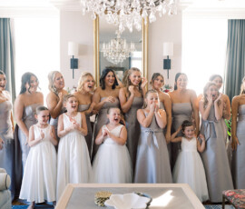 Bridesmaids in silver and flower girls in white laugh together in a bright, elegant room before a New Orleans wedding.