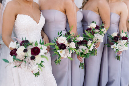 Bride in white lace and bridesmaids in lavender hold bouquets at a classic Louisiana wedding; faces not shown.