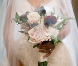Bride in lace dress holds white, pink, and burgundy bouquet under a sheer veil—romantic New Orleans wedding inspiration.