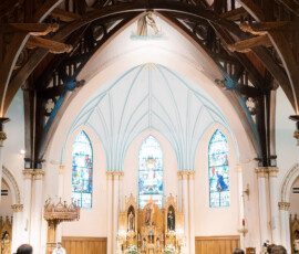 Bride and groom at the altar in a grand New Orleans church with stained glass, pews, and guests watching.