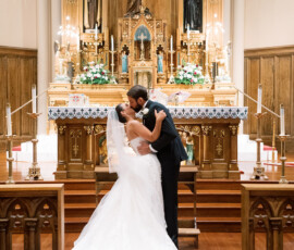 Bride and groom kiss at an ornate New Orleans church altar, surrounded by candles and religious statues after their ceremony.