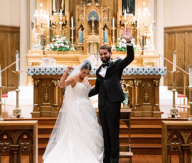 Bride and groom celebrate at a New Orleans church altar, smiling and holding hands; she wears a white gown, he’s in a tuxedo.