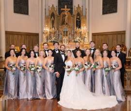 Bride and groom with bridesmaids in silver and groomsmen in black tuxedos pose, smiling, at a New Orleans church wedding.