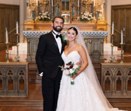 Bride and groom smile with a bouquet in a Louisiana church, ornate altar behind them during their wedding ceremony.