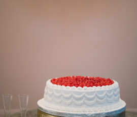 White cake with red berries on gold stand, candles, and champagne flutes on glass table evoke a Louisiana wedding.